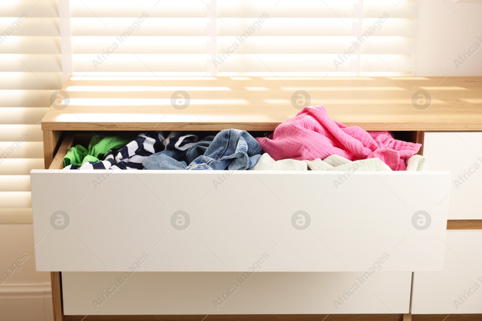 Photo of Cluttered chest of drawers indoors. Clothes in mess