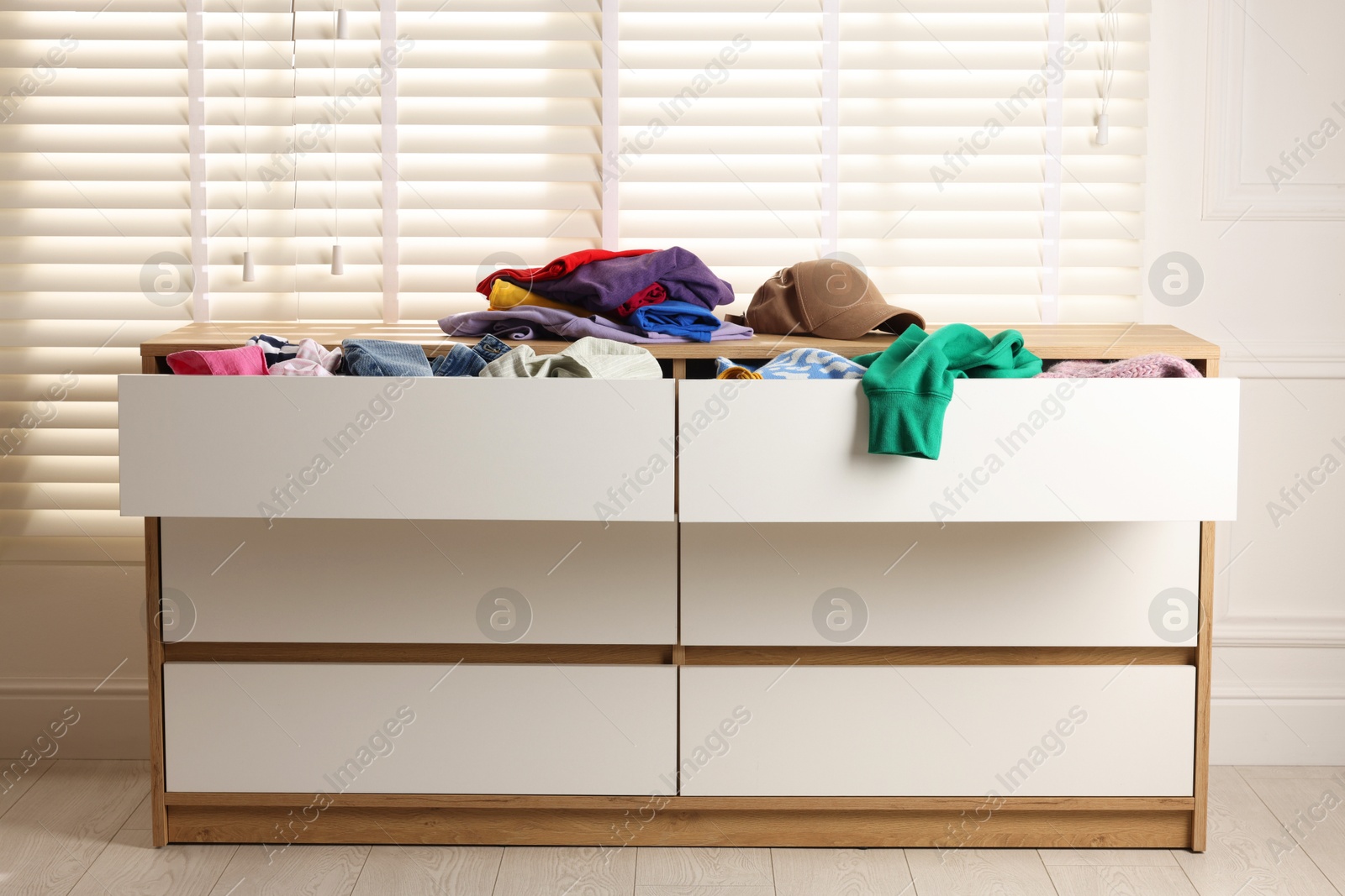 Photo of Cluttered chest of drawers indoors. Clothes in mess