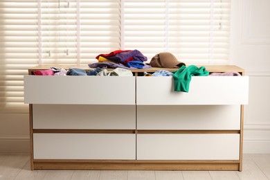 Cluttered chest of drawers indoors. Clothes in mess