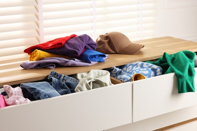 Cluttered chest of drawers indoors, closeup. Clothes in mess