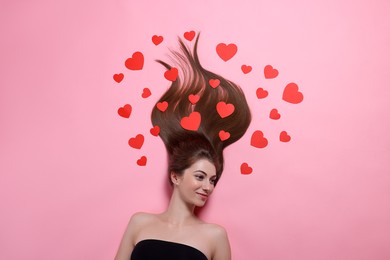 Beautiful young woman with long hair and red paper hearts on pink background, top view