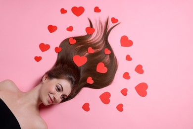 Beautiful young woman with long hair and red paper hearts on pink background, top view