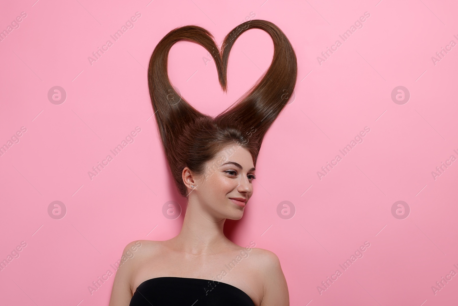 Photo of Beautiful young woman with hair in shape of heart on pink background, top view