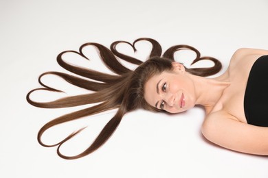 Beautiful young woman with hair in shape of hearts on white background