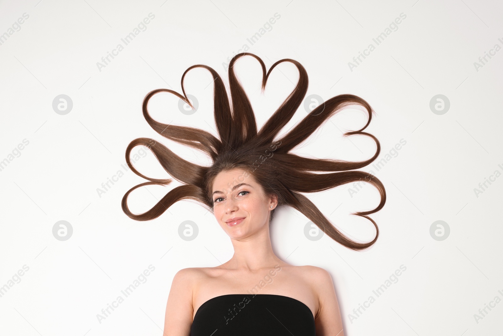 Photo of Beautiful young woman with hair in shape of hearts on white background, top view