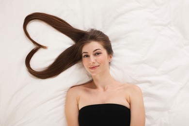 Photo of Beautiful young woman with hair in shape of heart on bed, top view