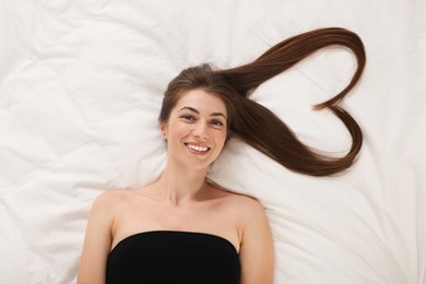 Photo of Beautiful young woman with hair in shape of heart on bed, top view