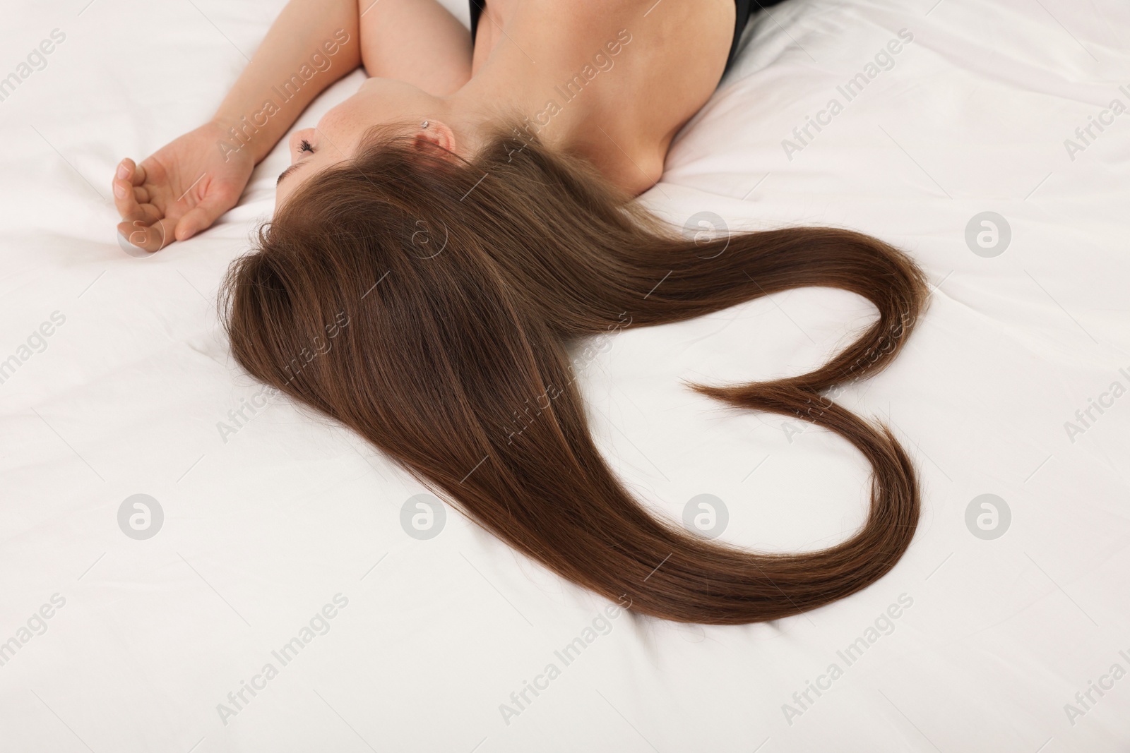 Photo of Young woman with beautiful hair in shape of heart on bed