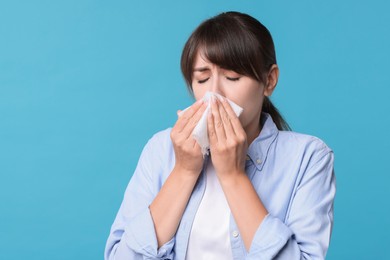 Photo of Woman with napkin suffering from sinusitis on light blue background. Space for text