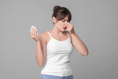 Woman with napkin suffering from sinusitis on grey background