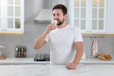 Photo of Handsome man drinking water with lemon in kitchen