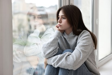 Photo of Loneliness concept. Sad teenage girl near window at home