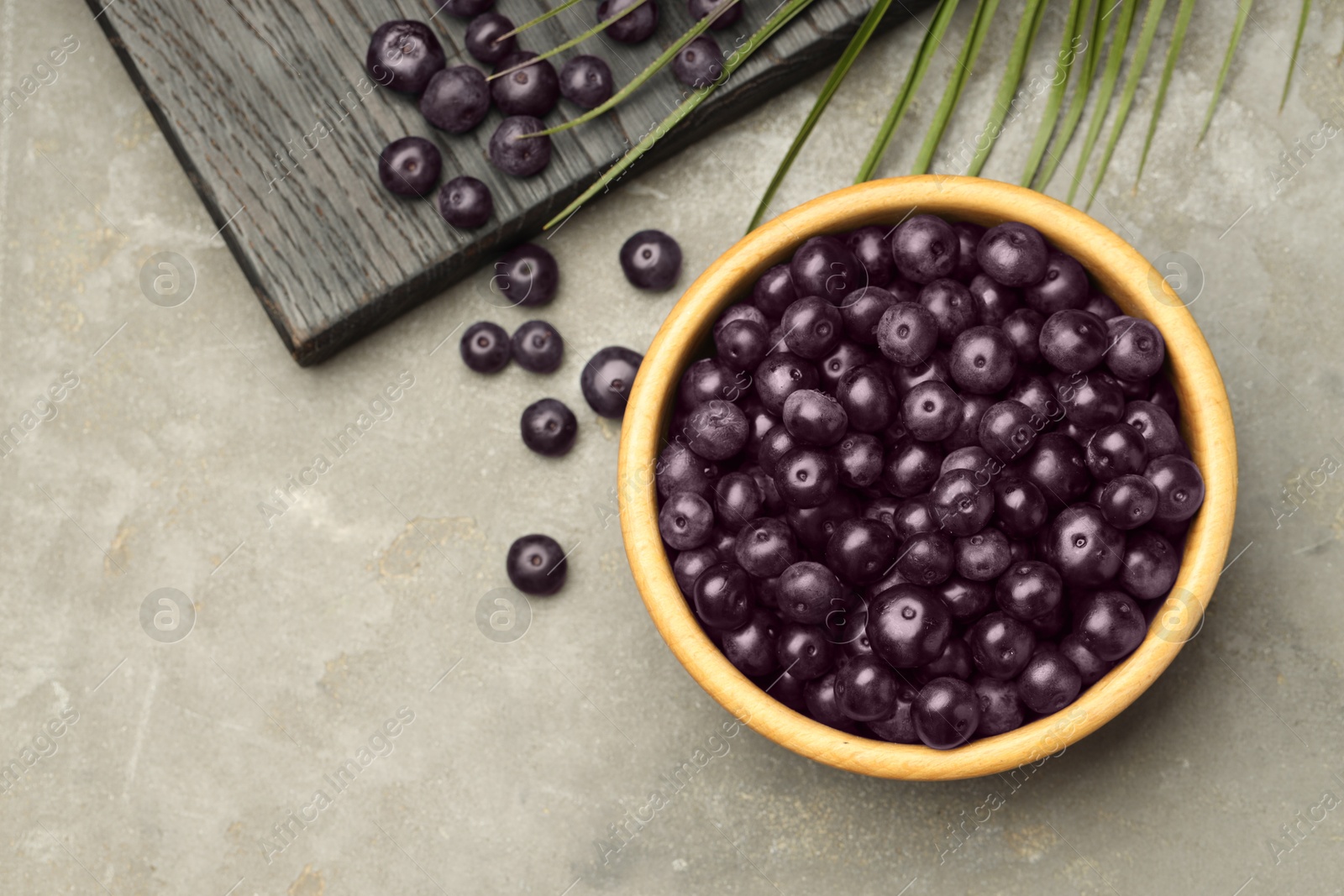 Photo of Ripe acai berries in bowl on grey textured table, flat lay. Space for text