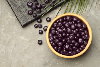 Photo of Ripe acai berries in bowl on grey textured table, flat lay. Space for text