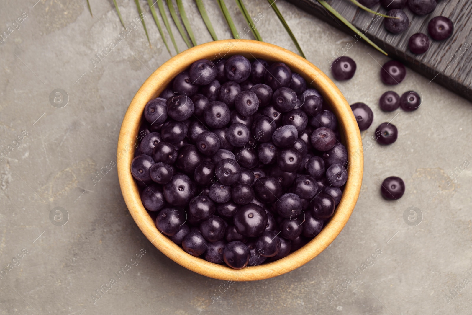 Photo of Ripe acai berries in bowl on grey textured table, flat lay