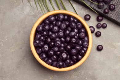 Ripe acai berries in bowl on grey textured table, flat lay