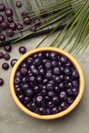 Photo of Ripe acai berries in bowl on grey textured table, flat lay