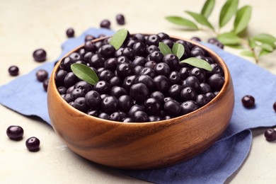 Photo of Ripe acai berries and leaves in bowl on grey table, closeup