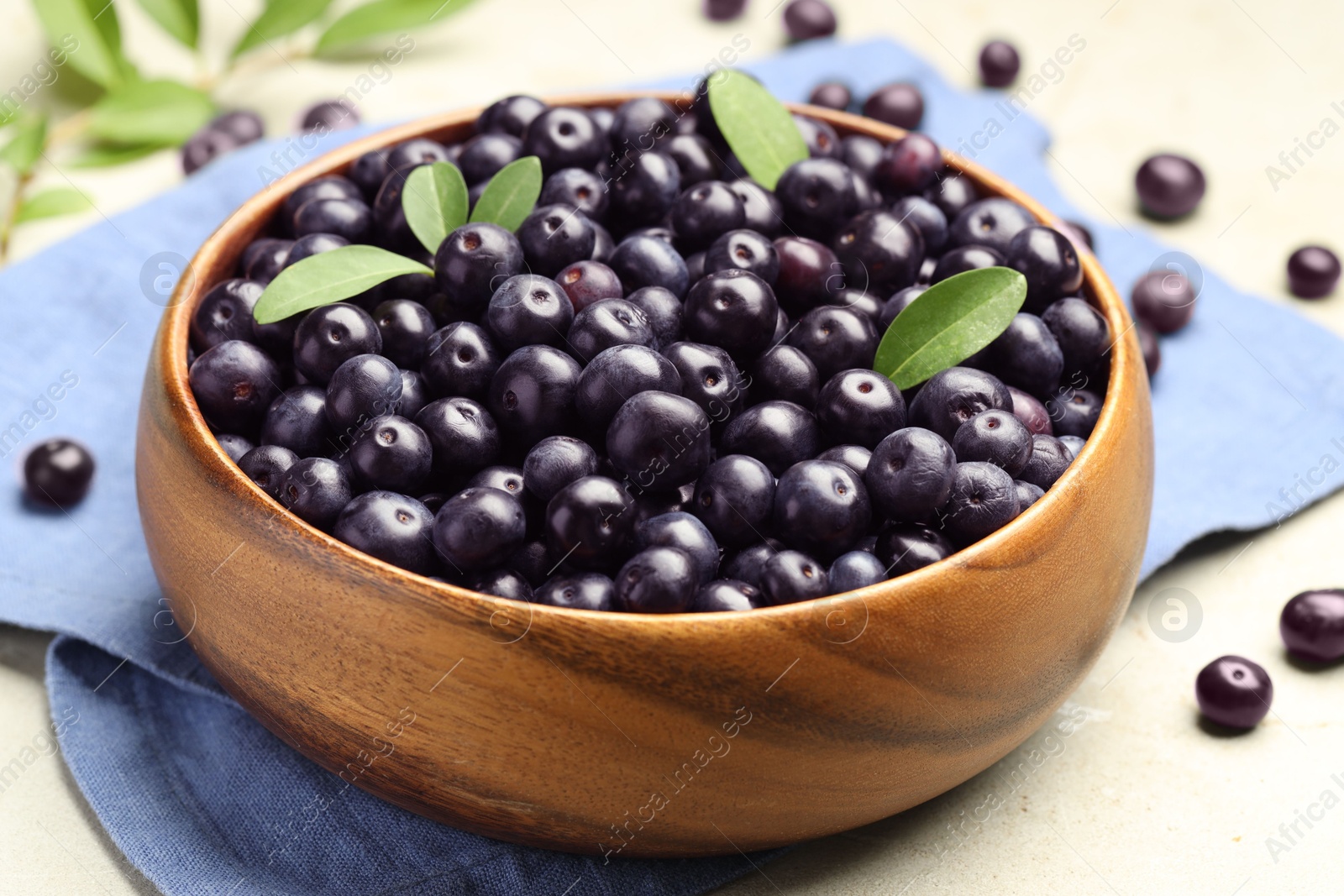 Photo of Ripe acai berries and leaves in bowl on grey table, closeup