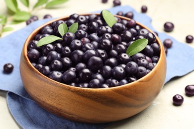 Photo of Ripe acai berries and leaves in bowl on grey table, closeup