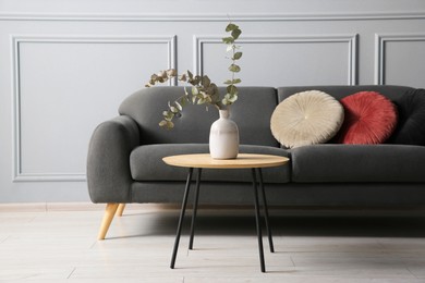 Stylish sofa with cushions and eucalyptus branches in vase on coffee table in room