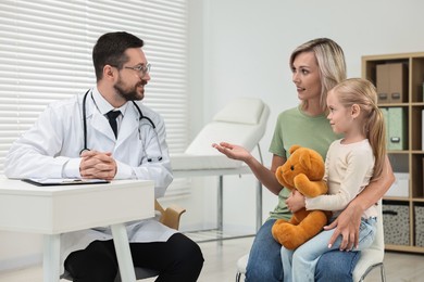 Doctor consulting little girl with teddy bear and her mother in hospital