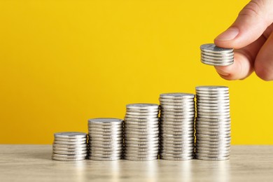 Photo of Woman putting coins at wooden table against yellow background, closeup. Salary concept