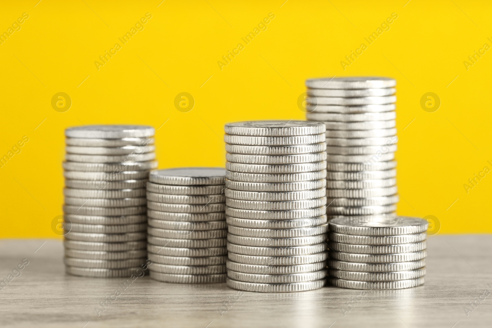 Photo of Stacked coins on wooden table against yellow background, closeup. Salary concept