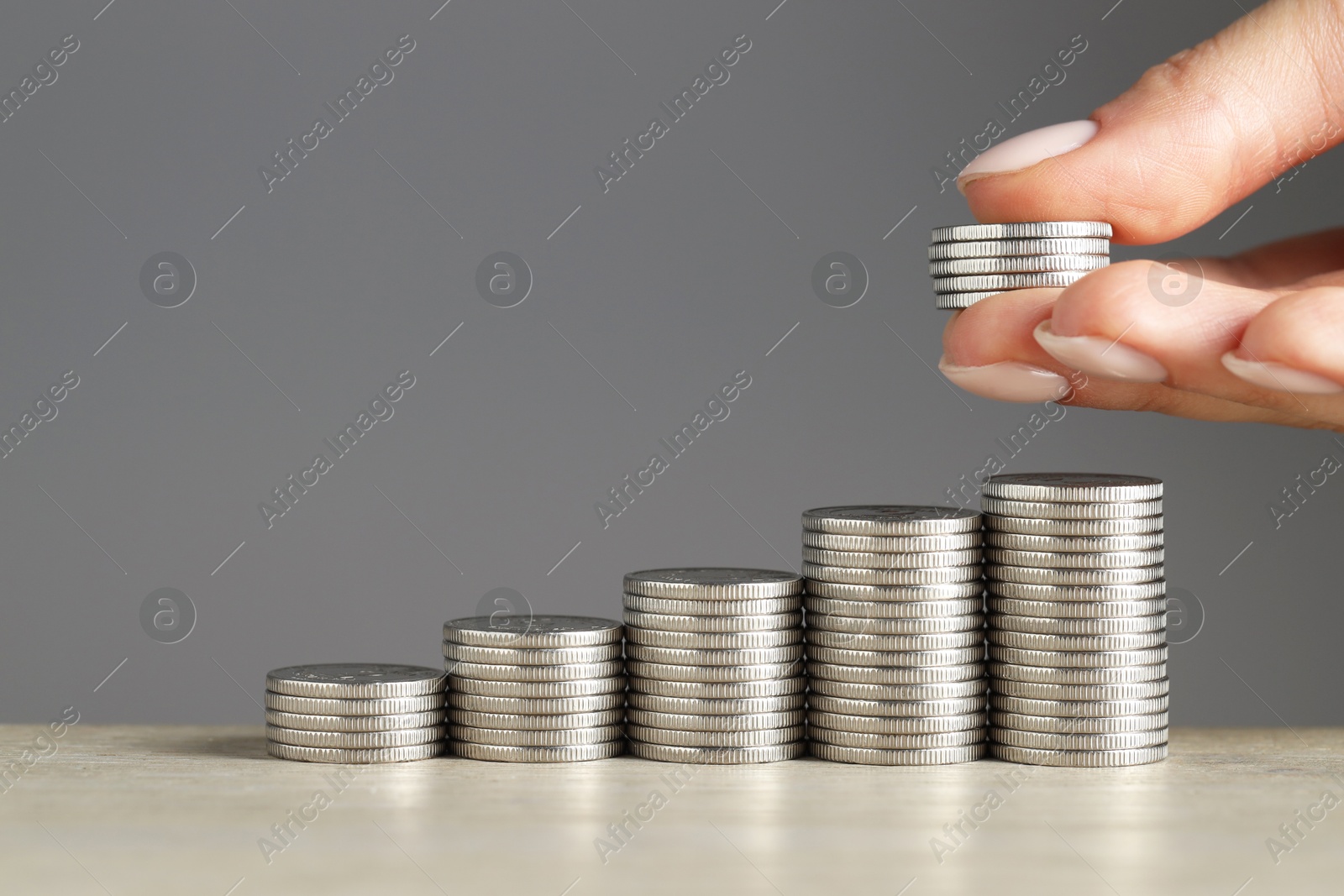 Photo of Woman putting coins at wooden table against grey background, closeup. Salary concept