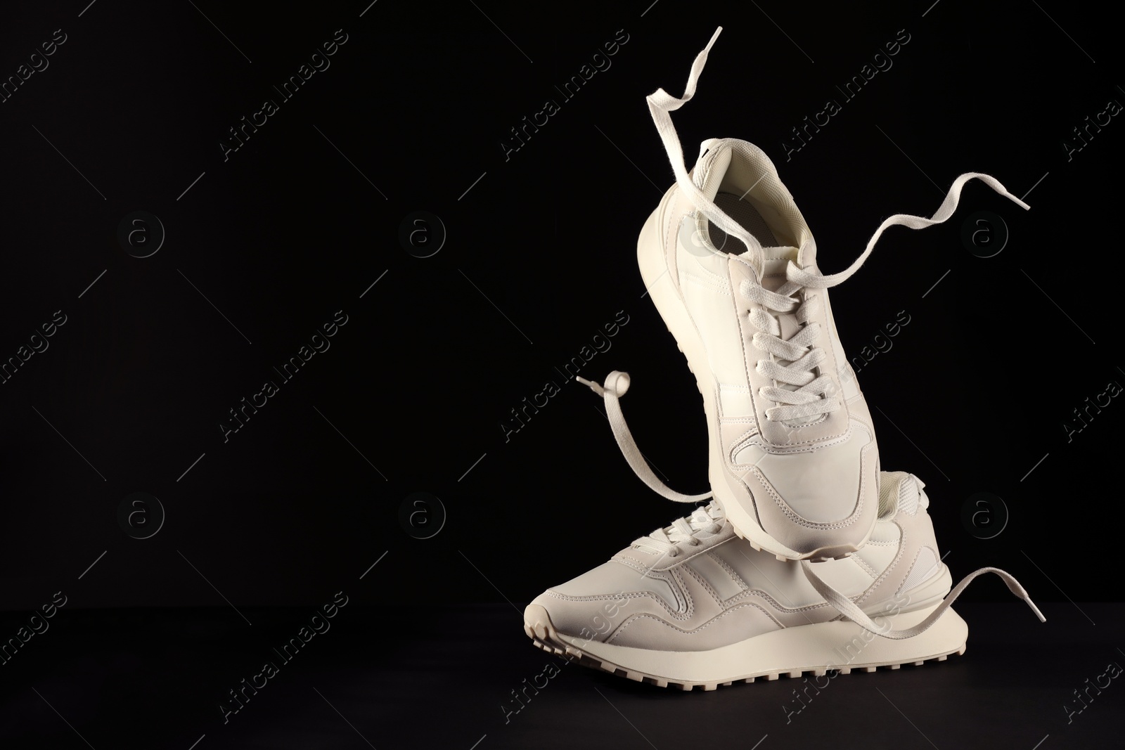 Photo of Pair of stylish sneakers in air against black background, space for text