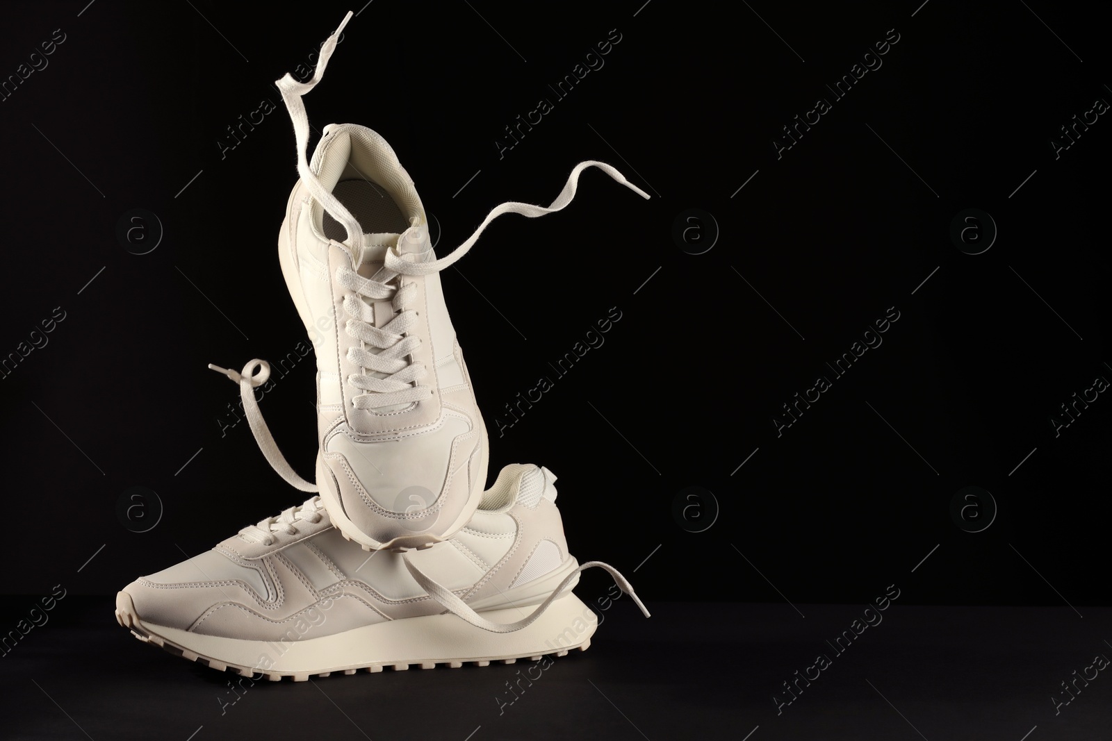 Photo of Pair of stylish sneakers in air against black background, space for text