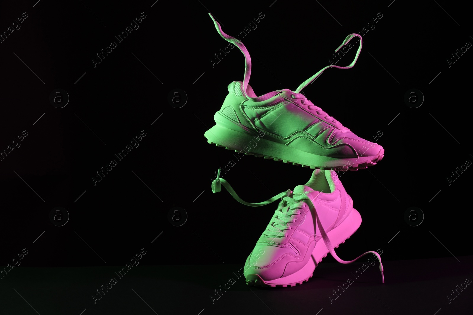 Photo of Pair of stylish sneakers in air against dark background in neon lights, space for text