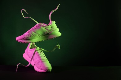 Pair of stylish sneakers in air against dark background in neon lights, space for text