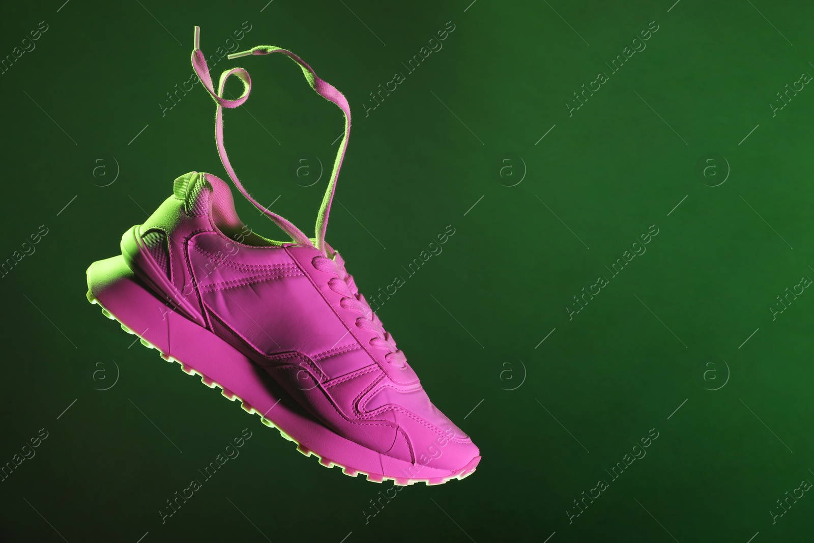 Photo of Stylish sneaker in air against dark green background in neon lights, space for text