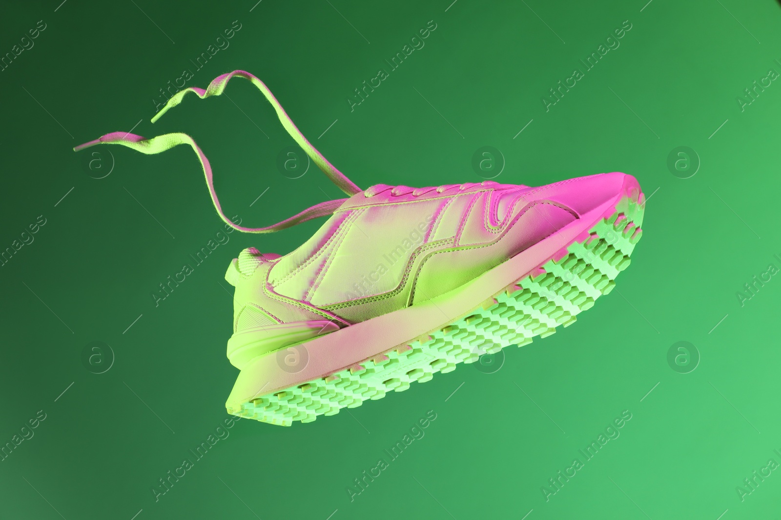 Photo of Stylish sneaker in air against green background in neon lights