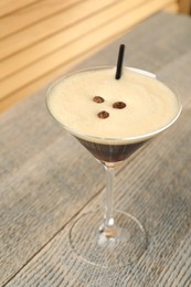 Photo of Delicious espresso martini with coffee beans in glass on wooden table