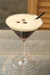 Photo of Delicious espresso martini with coffee beans in glass on wooden table