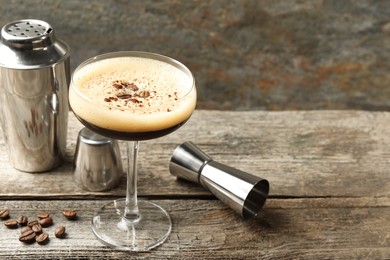 Delicious espresso martini with coffee beans in glass and bartender equipment on wooden table, space for text