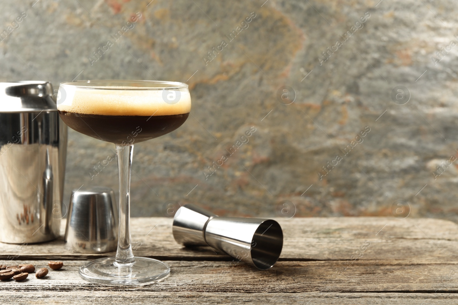 Photo of Delicious espresso martini with coffee beans in glass and bartender equipment on wooden table, space for text