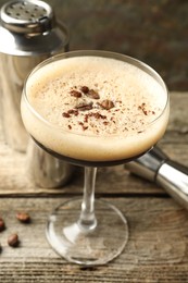 Delicious espresso martini with coffee beans in glass and bartender equipment on wooden table, closeup