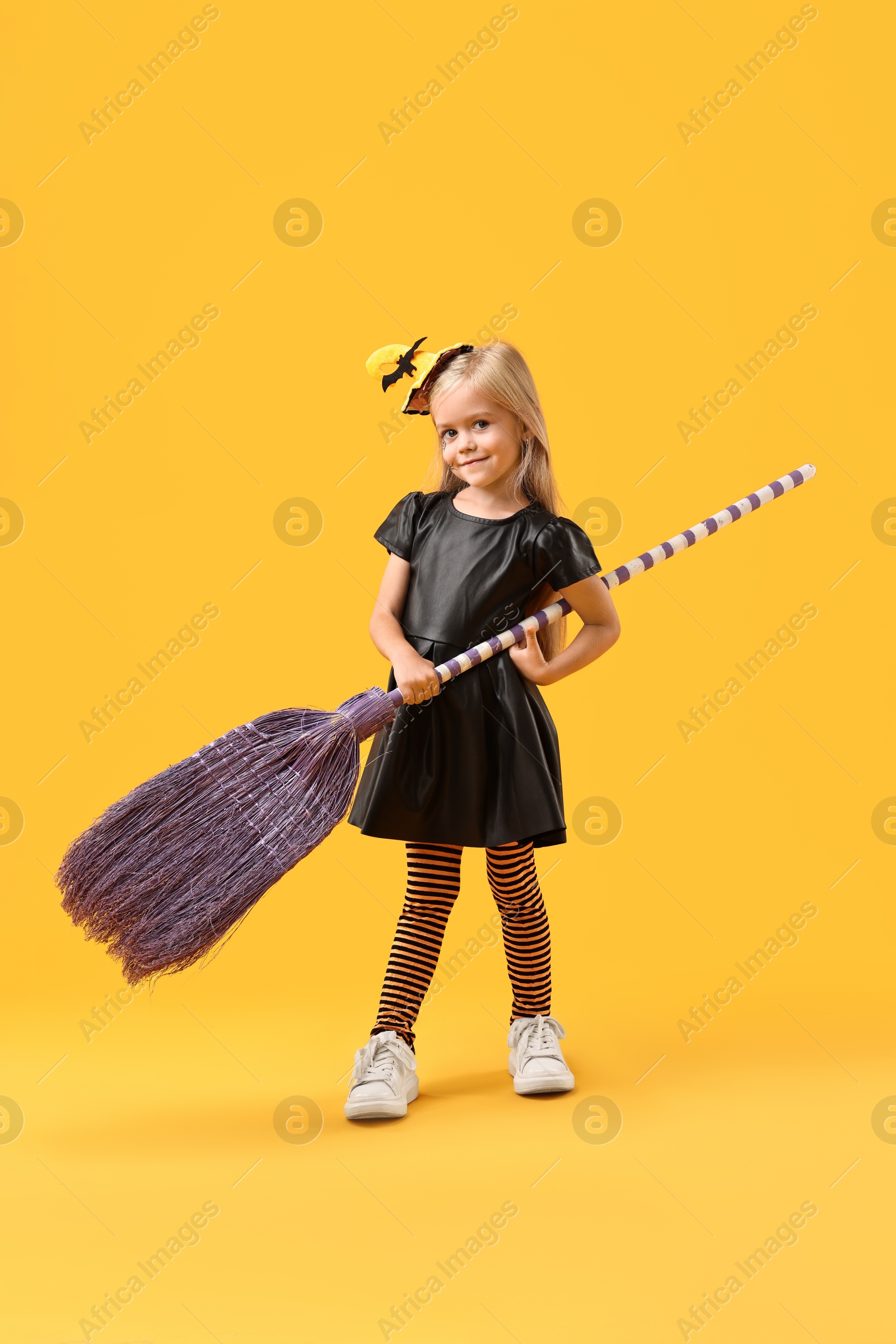 Photo of Funny girl with broom dressed like witch on yellow background. Halloween celebration