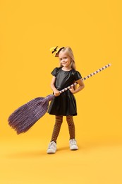 Funny girl with broom dressed like witch on yellow background. Halloween celebration