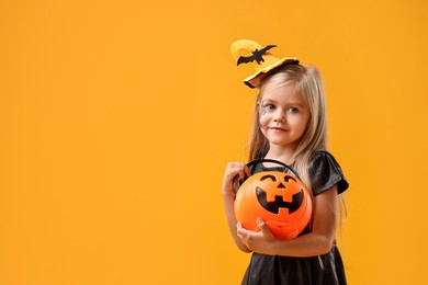 Cute girl with pumpkin bucket dressed like witch on yellow background, space for text. Halloween celebration