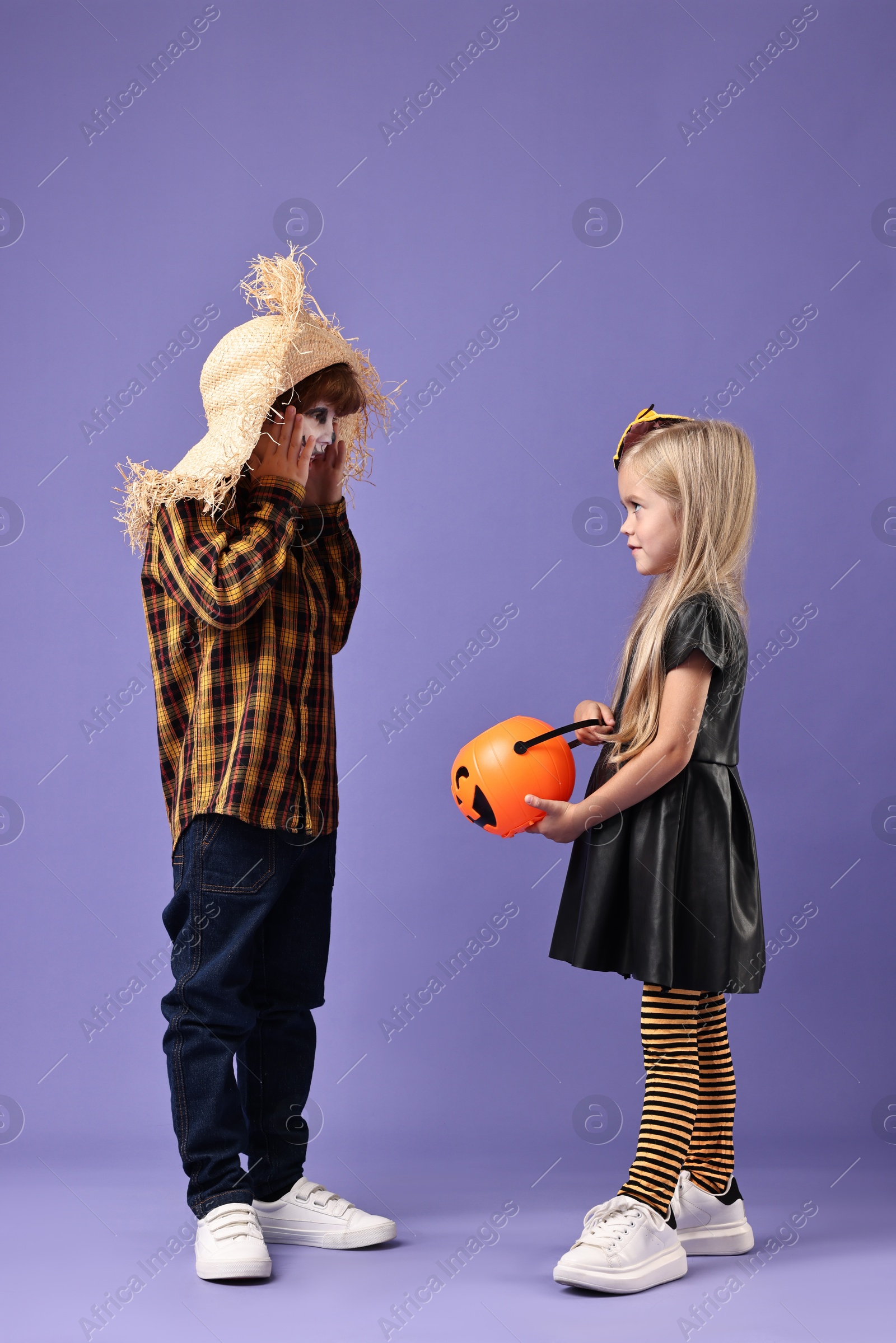 Photo of Cute children with pumpkin bucket wearing costumes on violet background. Halloween celebration