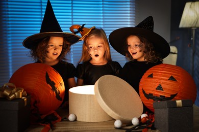 Surprised girls in costumes with festive decor and gift boxes indoors at night. Halloween celebration