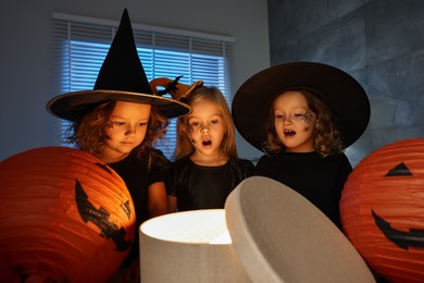 Surprised children in costumes with festive decor and gift box indoors at night. Halloween celebration