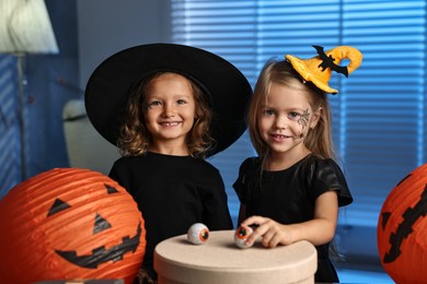 Photo of Cute children in costumes with festive decor and gift box indoors at night. Halloween celebration