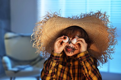 Photo of Boy with decorative eyeballs dressed like scarecrow indoors at night. Halloween celebration