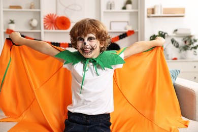 Funny boy dressed like pumpkin for Halloween celebration in room