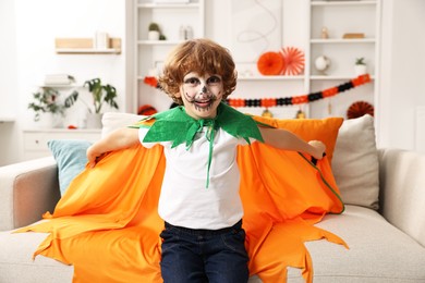 Photo of Funny boy dressed like pumpkin for Halloween celebration in room